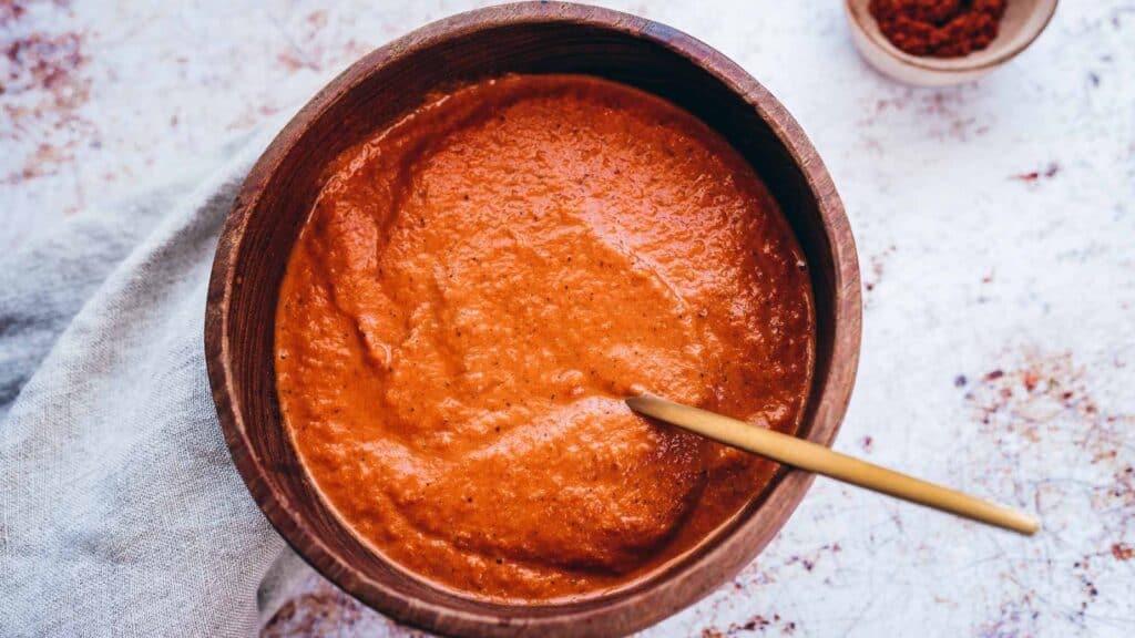 A small wooden bowl filled with a creamy red sauce with a gold spoon.