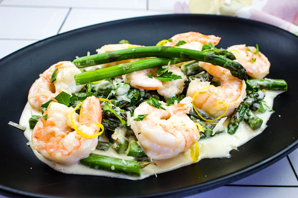 Shrimp & Asparagus Alfredo on a black plate.