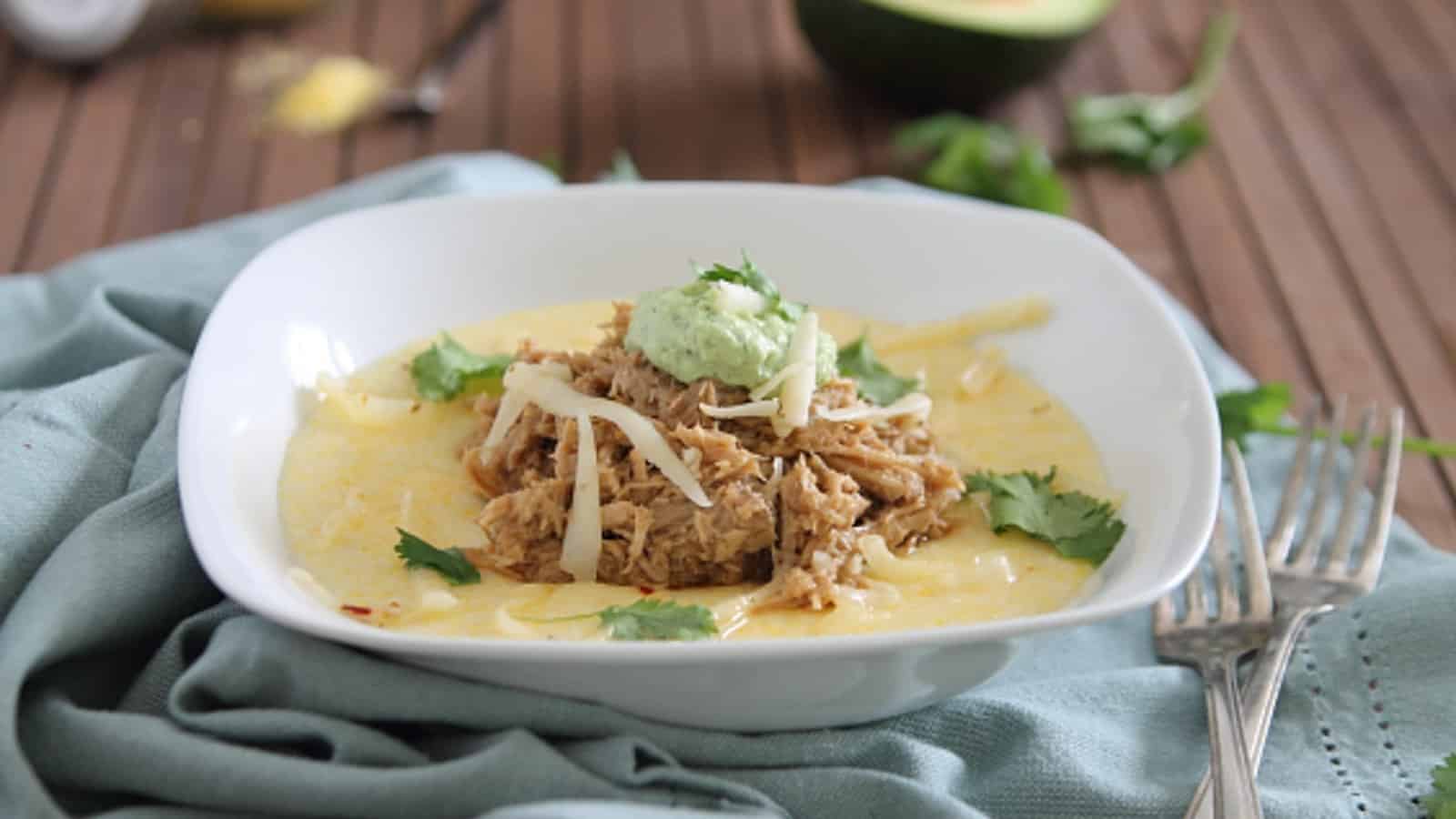 Slow cooker balsamic pulled pork over polenta with avocado crema in a white bowl.