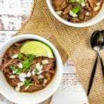 Two white bowls filled with slow cooker birria garnished with fresh lime wedges.