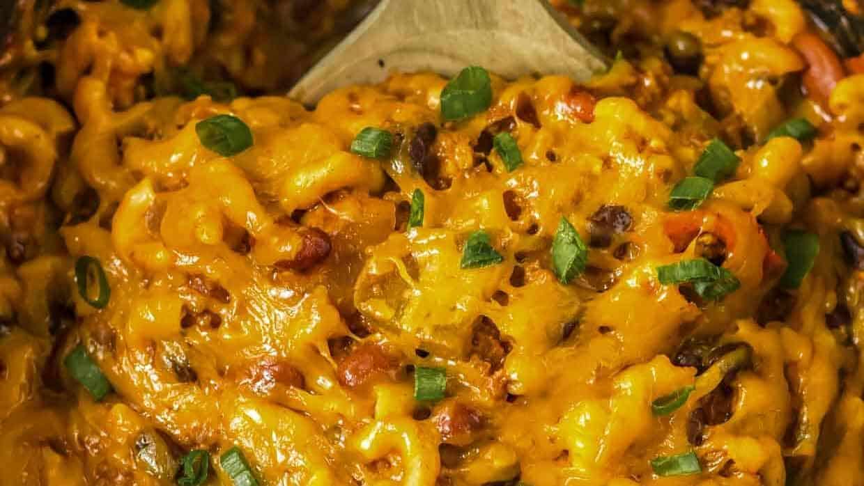 Cheese covered slow cooker chili mac in the crock pot with a wooden spoon.