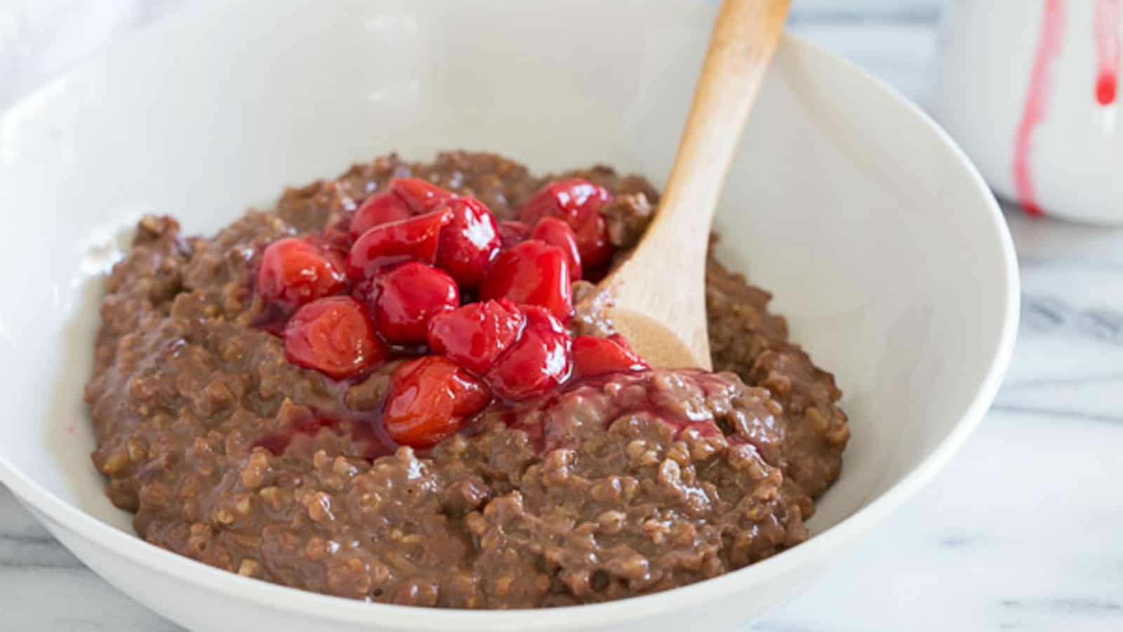 Slow cooker chocolate cherry steel cut oatmeal in a white bowl with a wooden spoon.