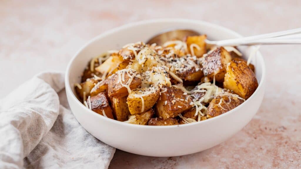 Cubed potatoes in a white bowl topped with shredded white cheese.