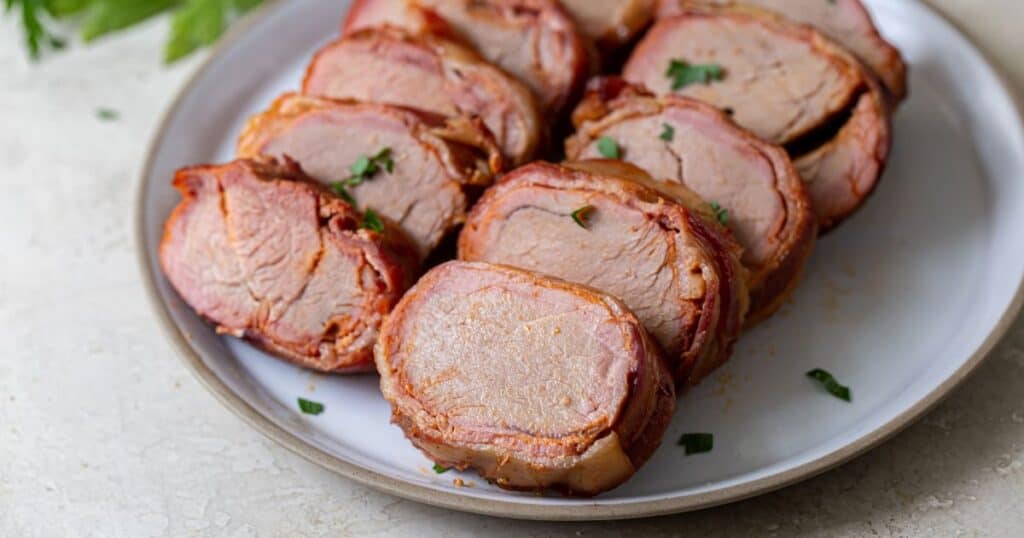 Sliced smoked bacon wrapped pork tenderloin on a plate.