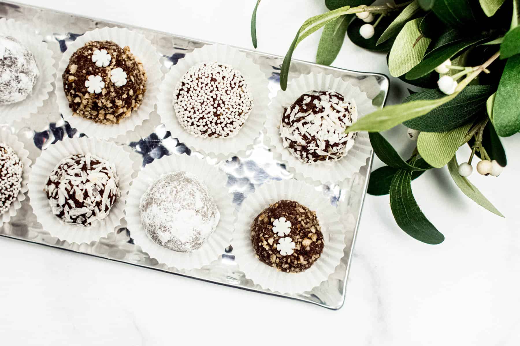 Spiced Rum Balls in a metal serving dish with winter greenery on a white marble surface.