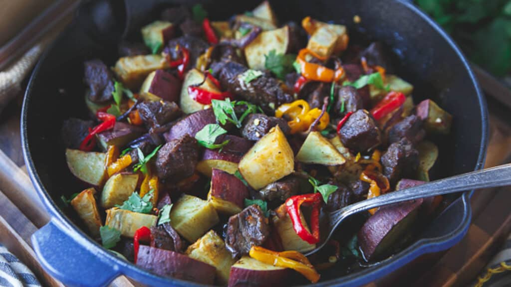 Steak peppers and potato skillet with a metal serving spoon.