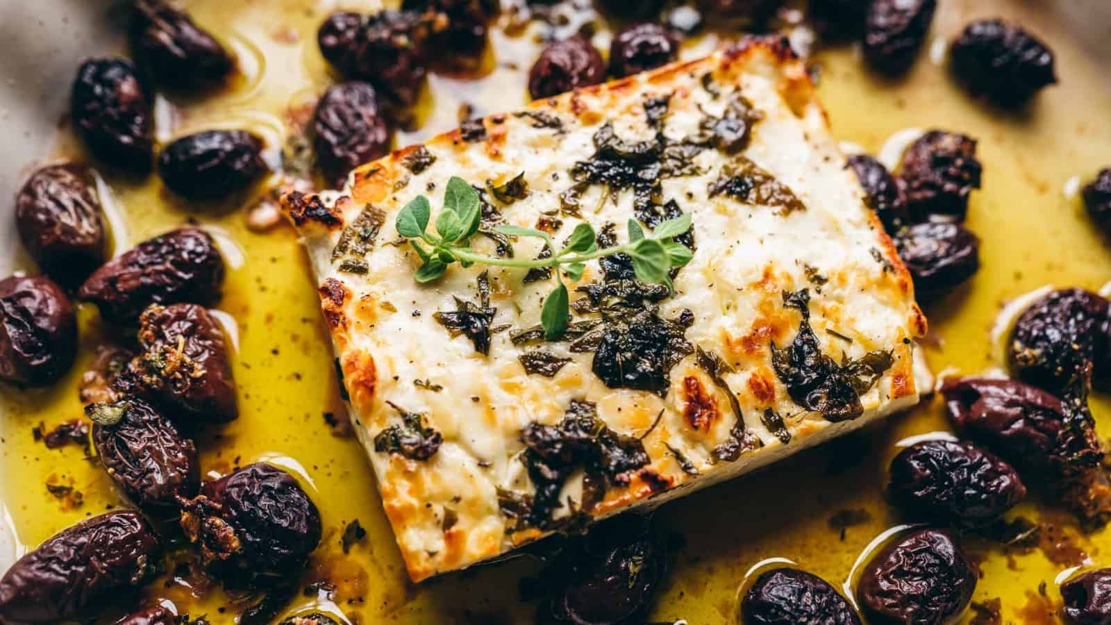 Close shot of a block of baked feta cheese topped with herbs.