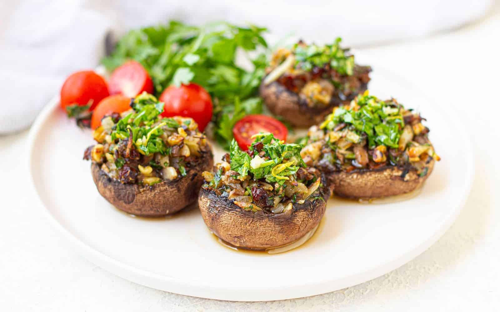 A white plate with vegan stuffed portobello mushrooms garnished with cherry tomatoes and parsley.