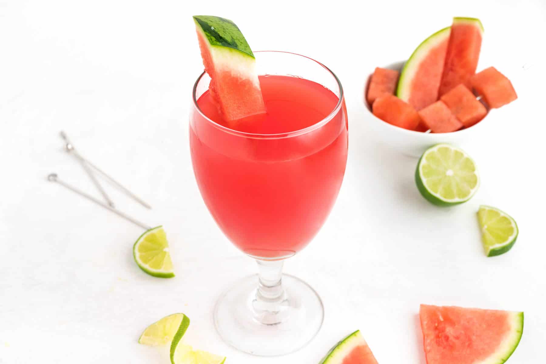 Watermelon and lime pieces surround a glass of a refreshing watermelon drink.