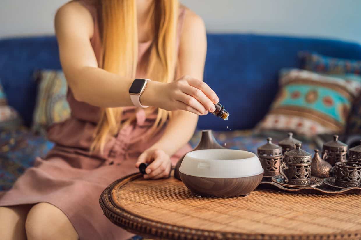 A picture of a woman adding essential oil to aroma diffuser on table.