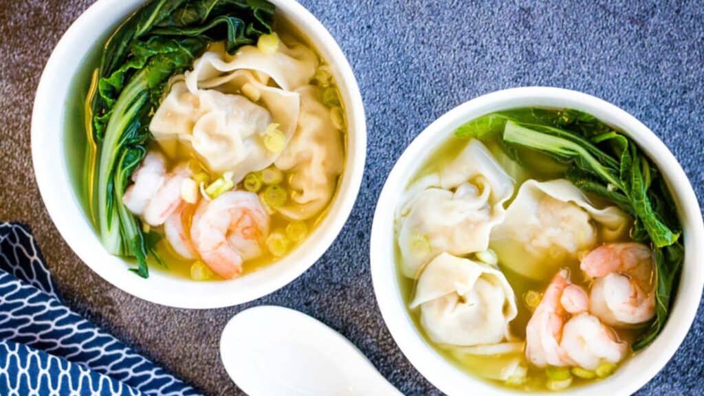 Two bowls of wonton soup with shrimp and greens.