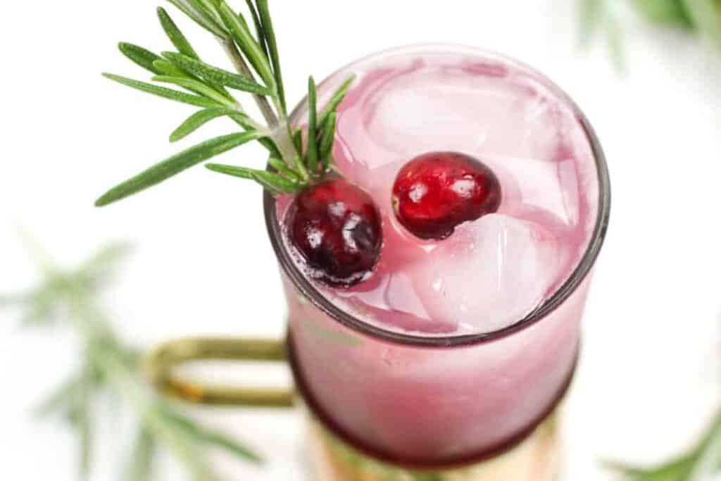 Cranberries on top of a cranberry cocktail in a copper mug.