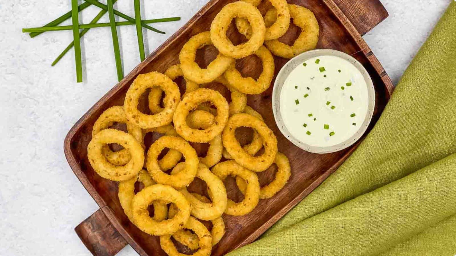 Onion rings on a wooden tray with dipping sauce.