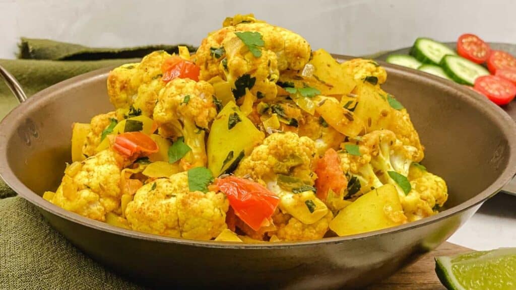 A bowl of cauliflower curry with tomatoes and cucumbers.