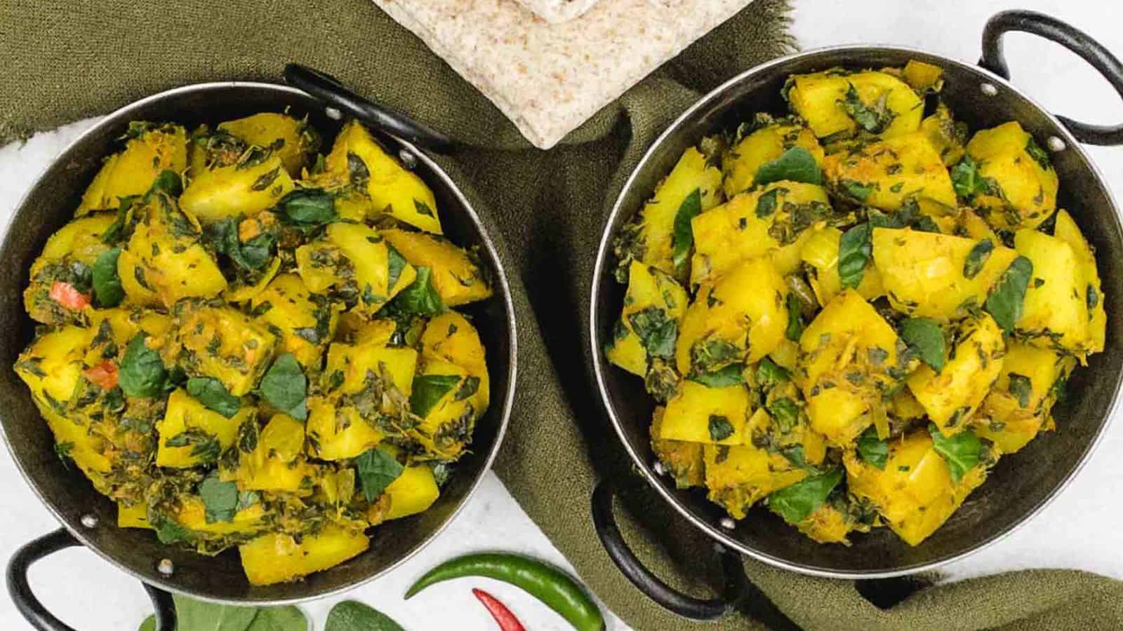 Two bowls of potato and spinach curry on a green cloth.