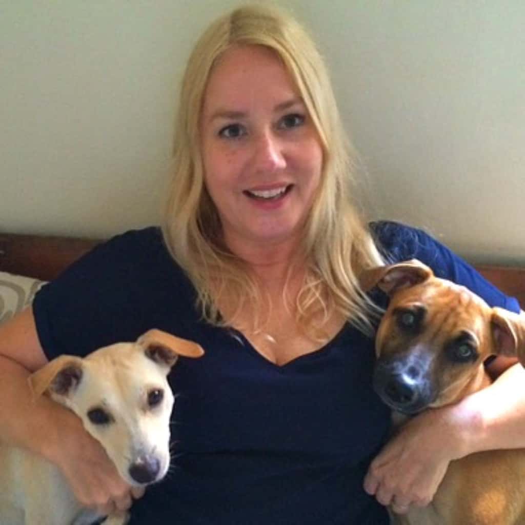 A woman is sitting on a bed with two dogs.