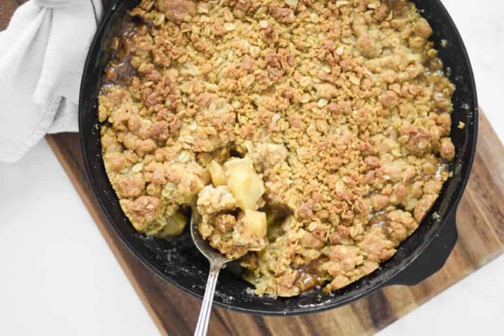 Apple crisp in a skillet with a spoon.