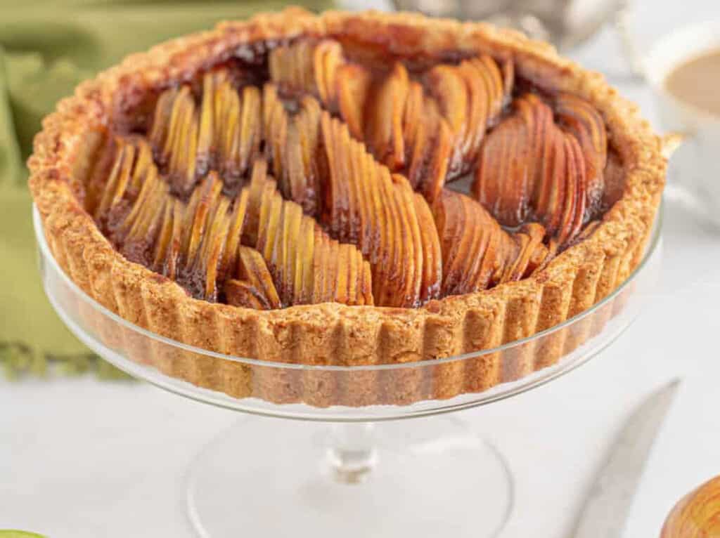 A tart with apples on top of a glass plate.