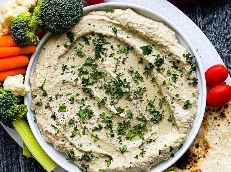 A bowl of eggplant dip with vegetables and pita chips.