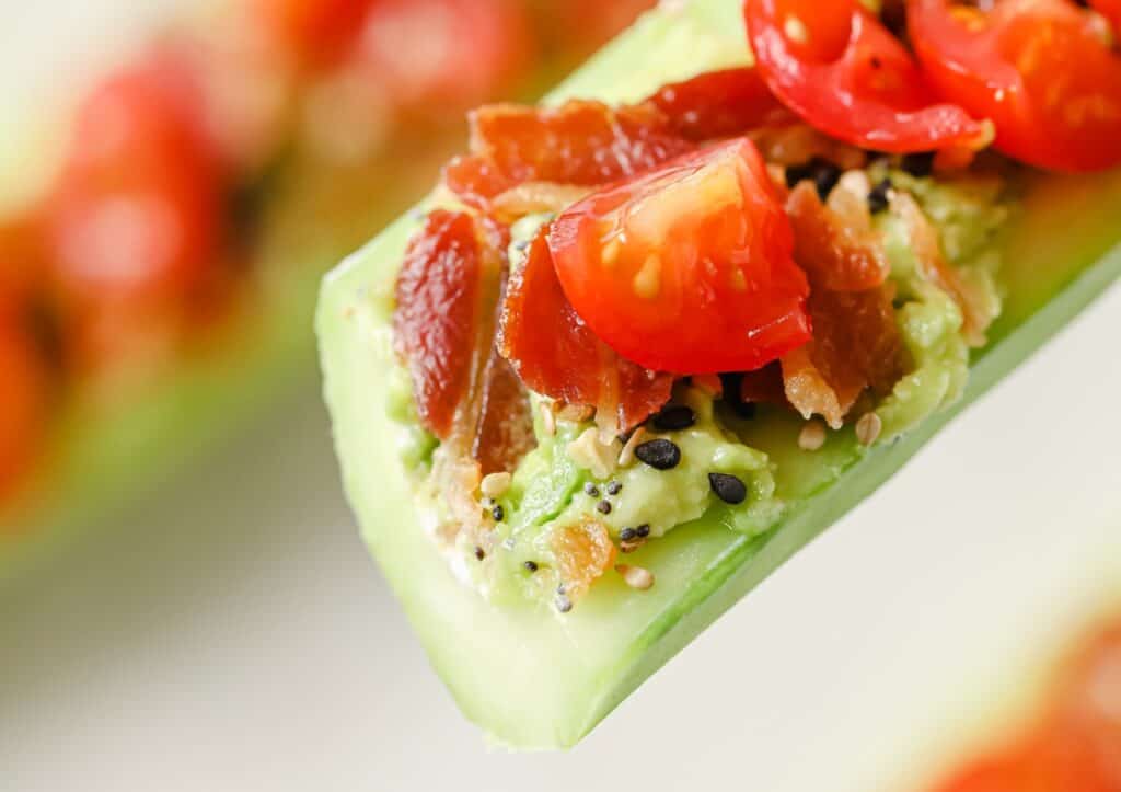 A cucumber boat with tomatoes and bacon on it.