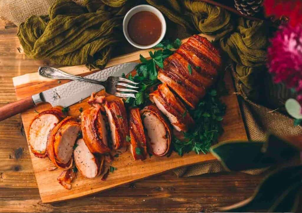 Sliced pork loin on a cutting board with a knife and fork.