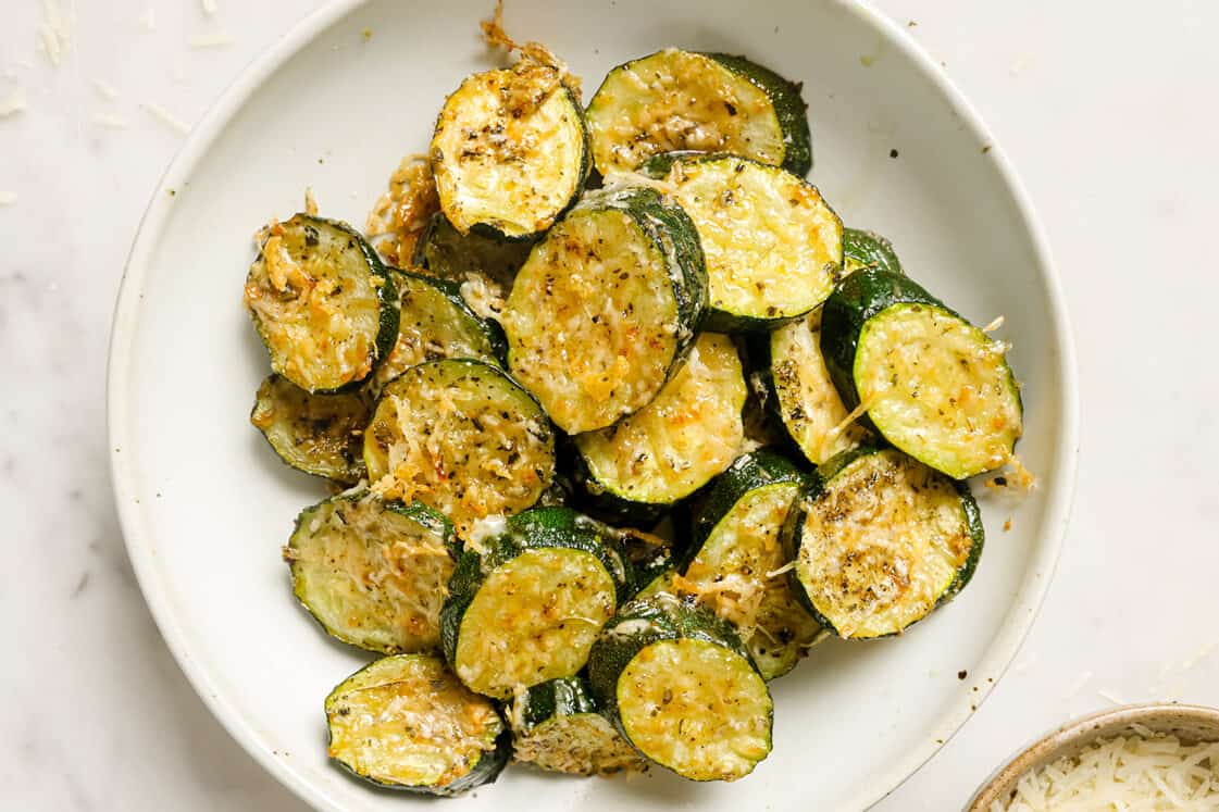 Baked sliced zucchini with parmesan on a white plate.
