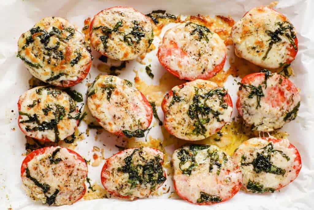 Baked tomatoes with cheese and basil on a baking sheet.
