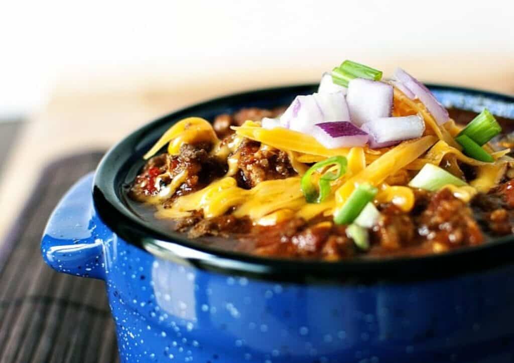 Chili in a blue bowl with onions and cheese.