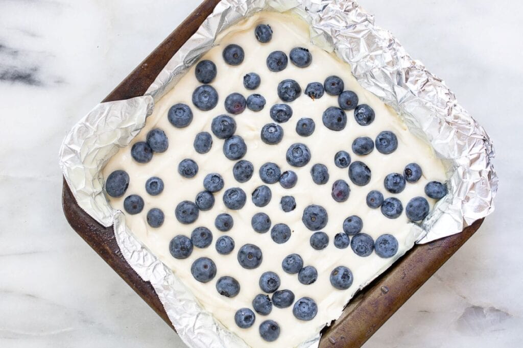 Blueberry cheesecake bars in a pan lined with foil.