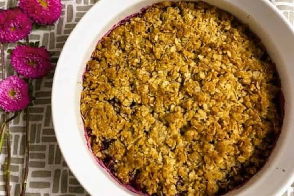 A warm dessert with a blueberry crumble on a white dish.