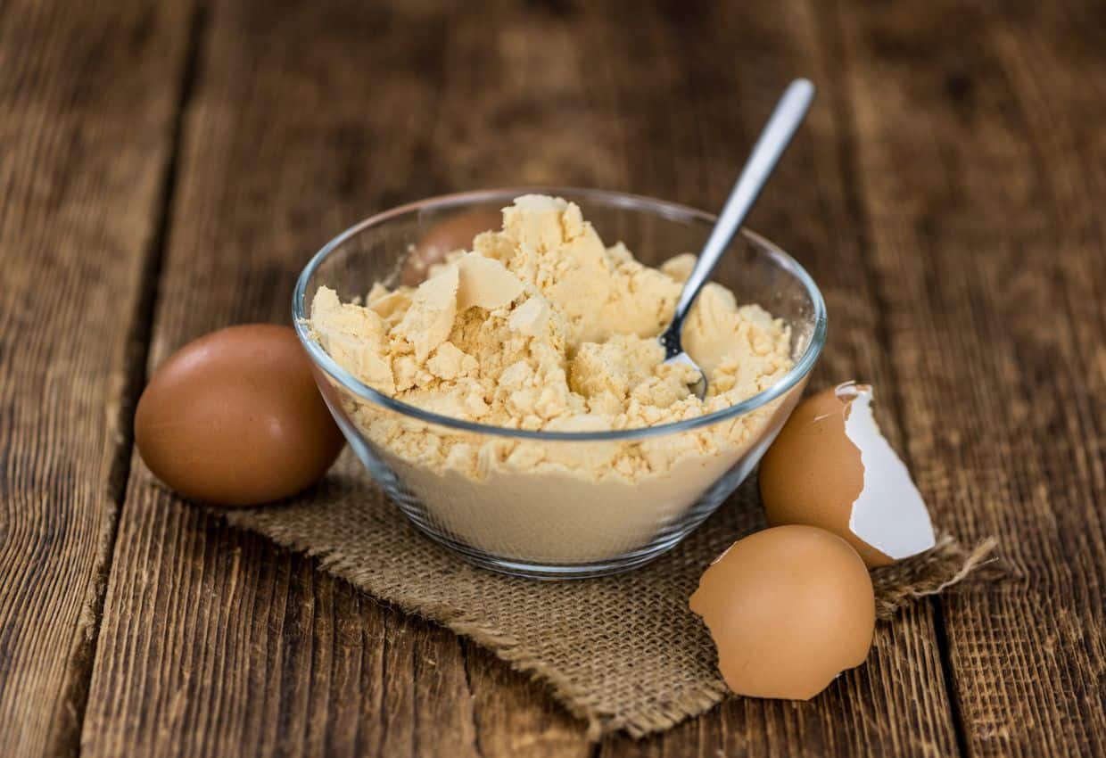 A bowl of egg powder and eggs on a wooden table.