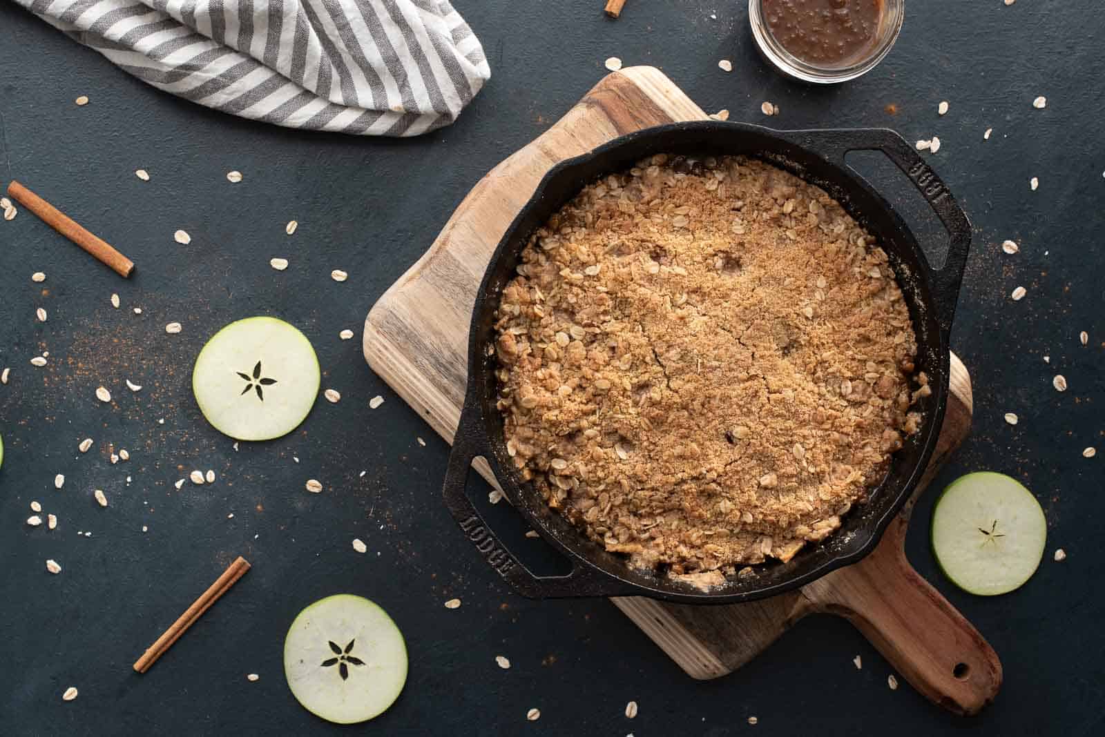 A butterscotch apple crumble in a cast iron skillet on a wooden cutting board.