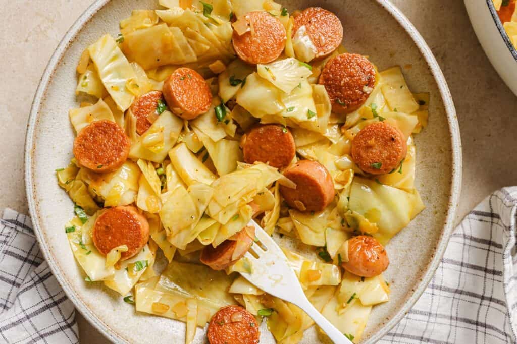 A fork in a bowl of cabbage and sausage.