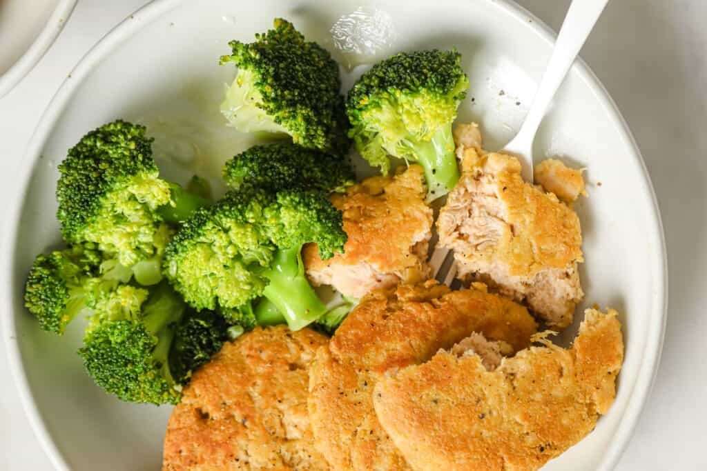 A white plate with broccoli and canned chicken patties.