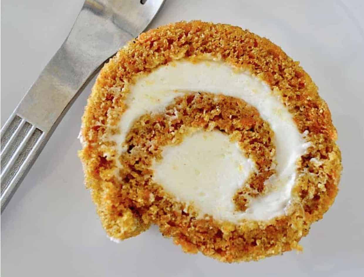 A slice of carrot cake on a plate with a fork.