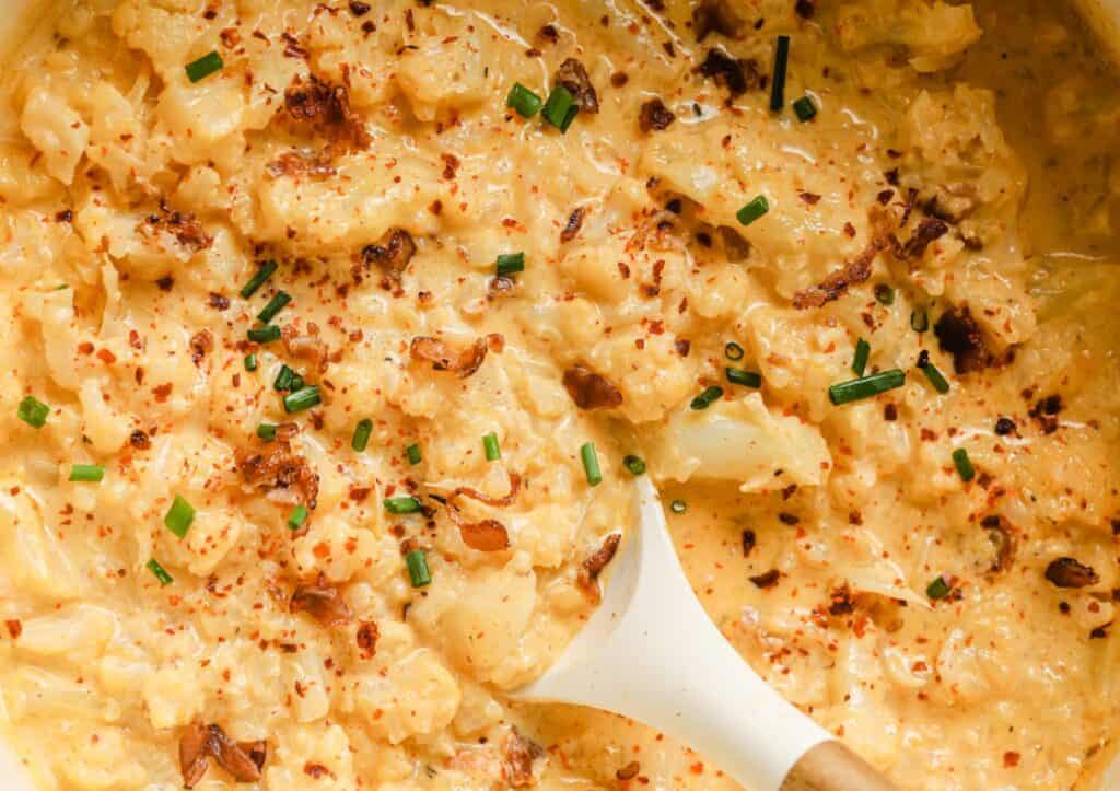 Cheesy cauliflower soup in a white bowl with a white spoon.