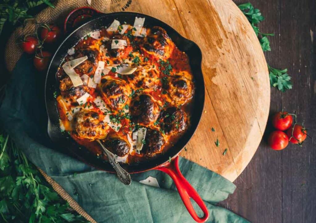 A skillet with meatballs and tomatoes on a wooden table.