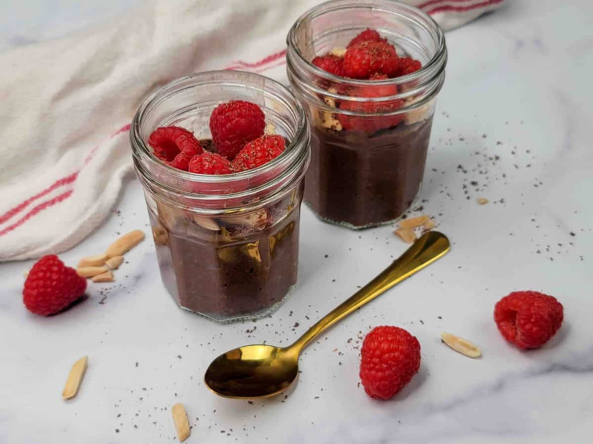 Two mason jars of chocolate chia pudding topped with sliced almonds and fresh raspberries.