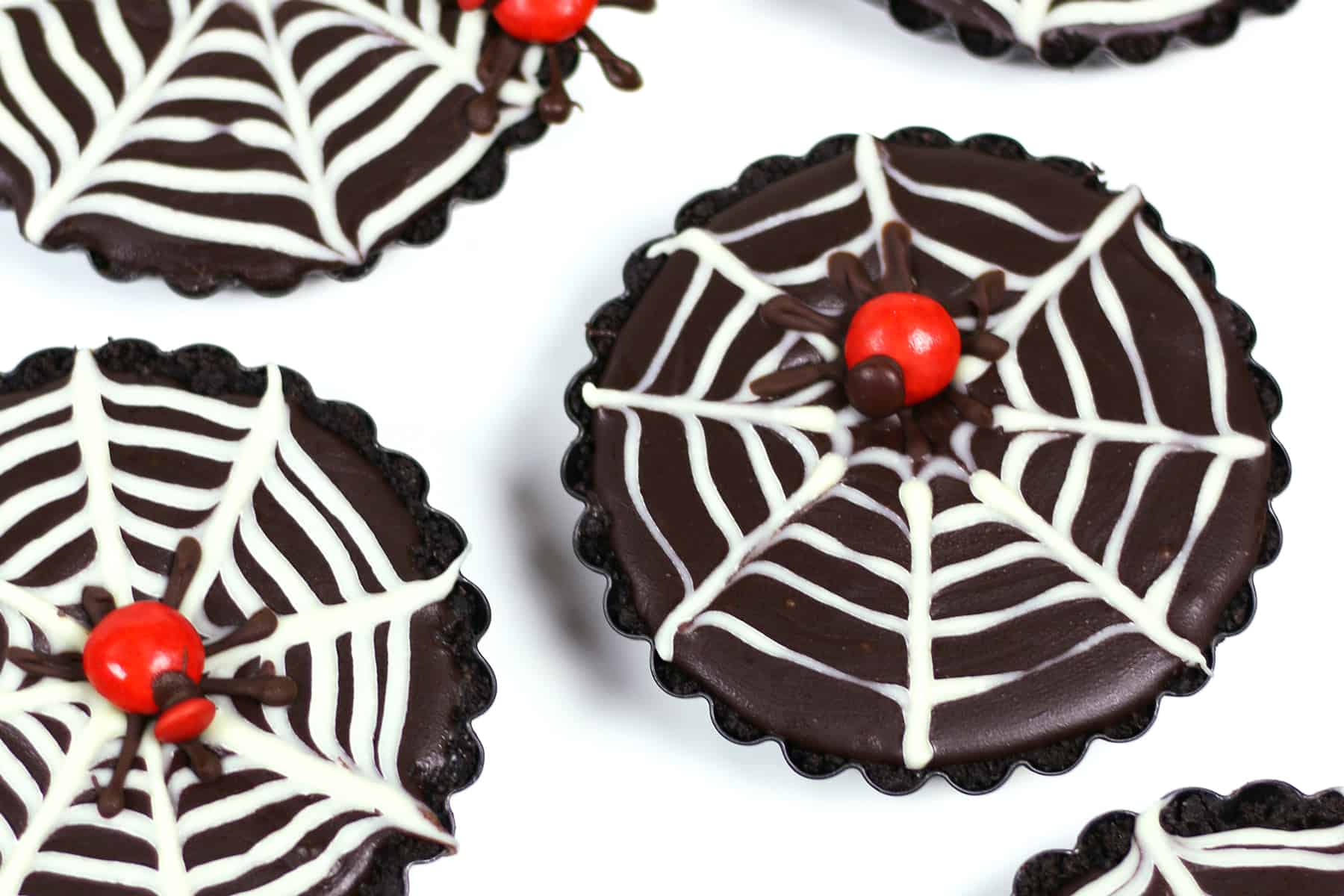 A group of chocolate spider web tarts on a white surface.