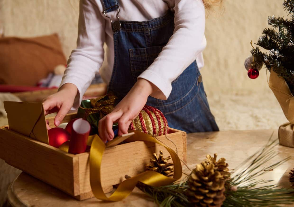 A girl is putting Christmas gifts and decorations in a wooden box.