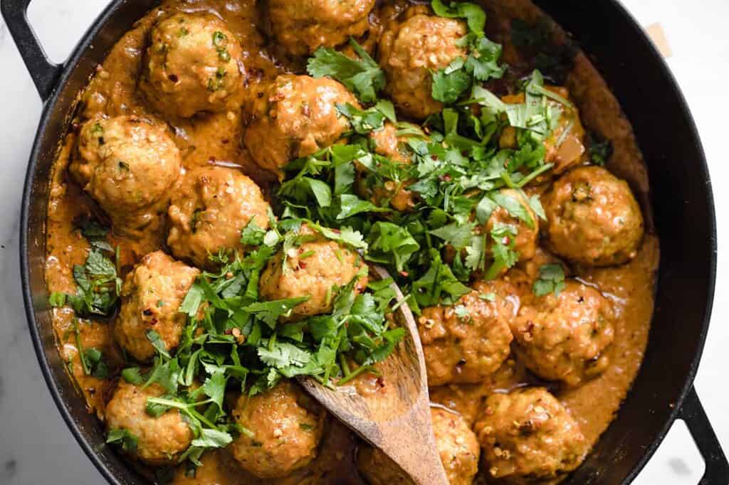 Thai turkey meatballs in a skillet with a wooden spoon.