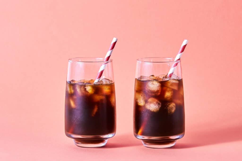 Two glasses of iced coffee on a pink background, showcasing the refreshingly chilled nature of the beverage.