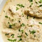 A white skillet of creamy garlic chicken garnished with herbs.