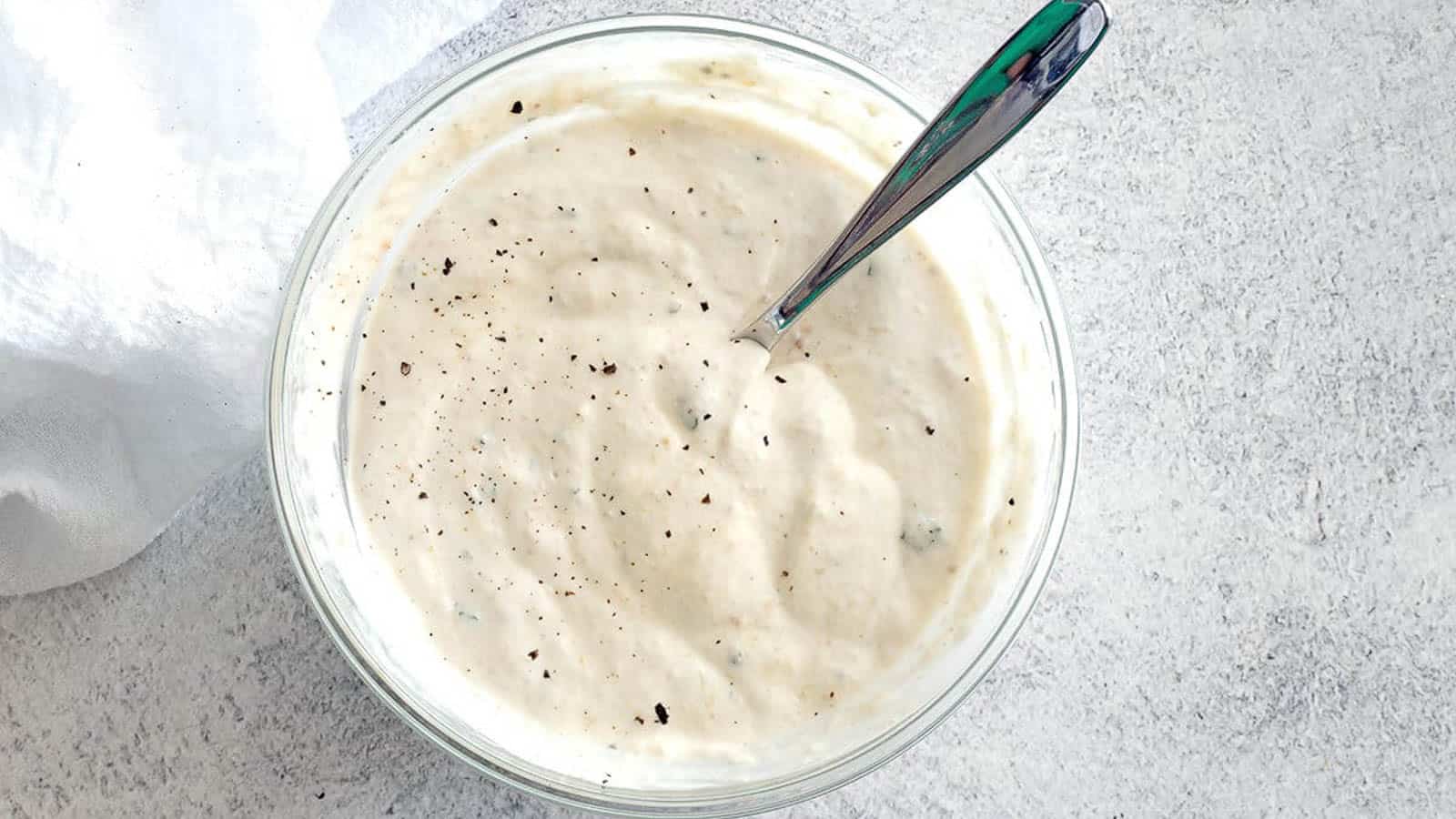 Horseradish sauce in a clear bowl with a silver spoon dipped inside.