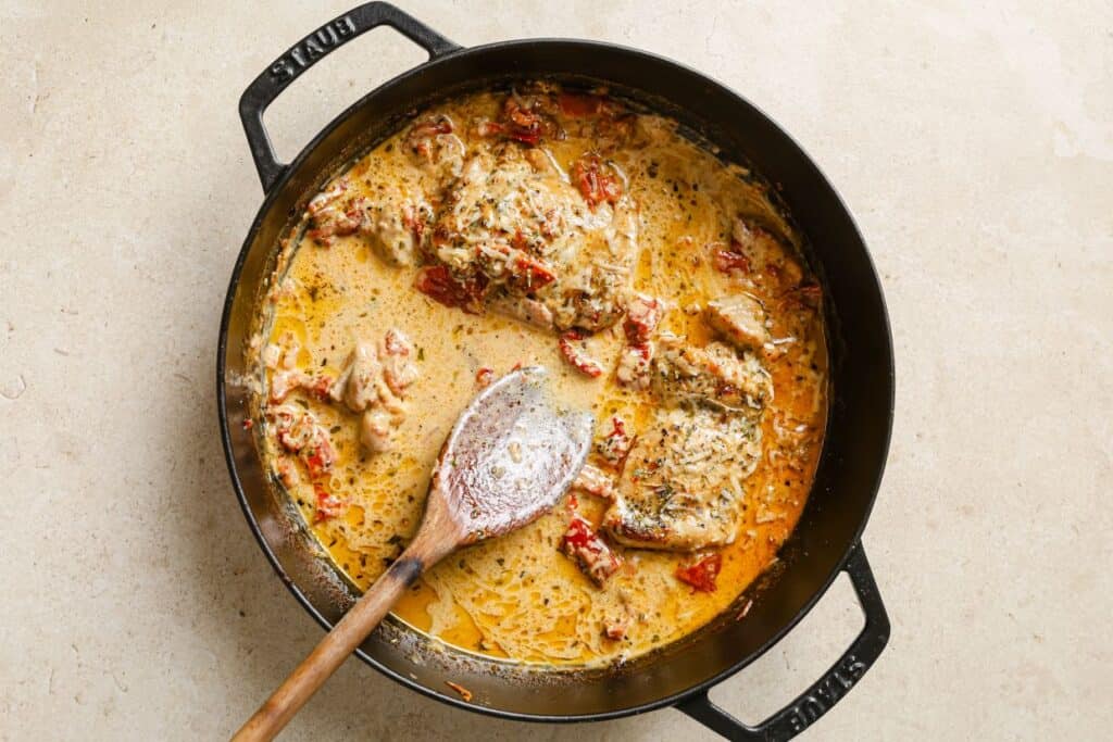 A skillet of creamy sun dried tomato chicken with a wooden spoon.