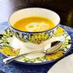 A bowl of butternut squash soup with a spoon on a colorful blue and white plate.