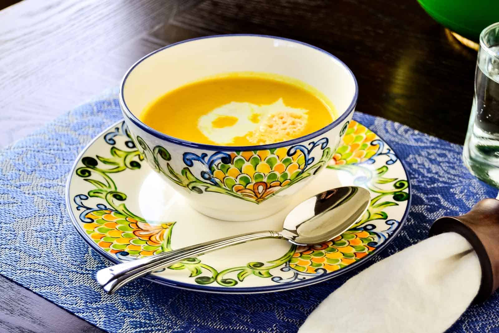 A bowl of butternut squash soup with a spoon on a colorful blue and white plate.