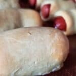 Image shows Hot dogs wrapped in crescent roll dough on a baking sheet.