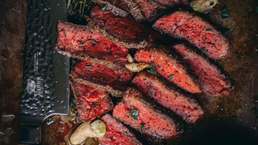 Steak on a cutting board with garlic and herbs.
