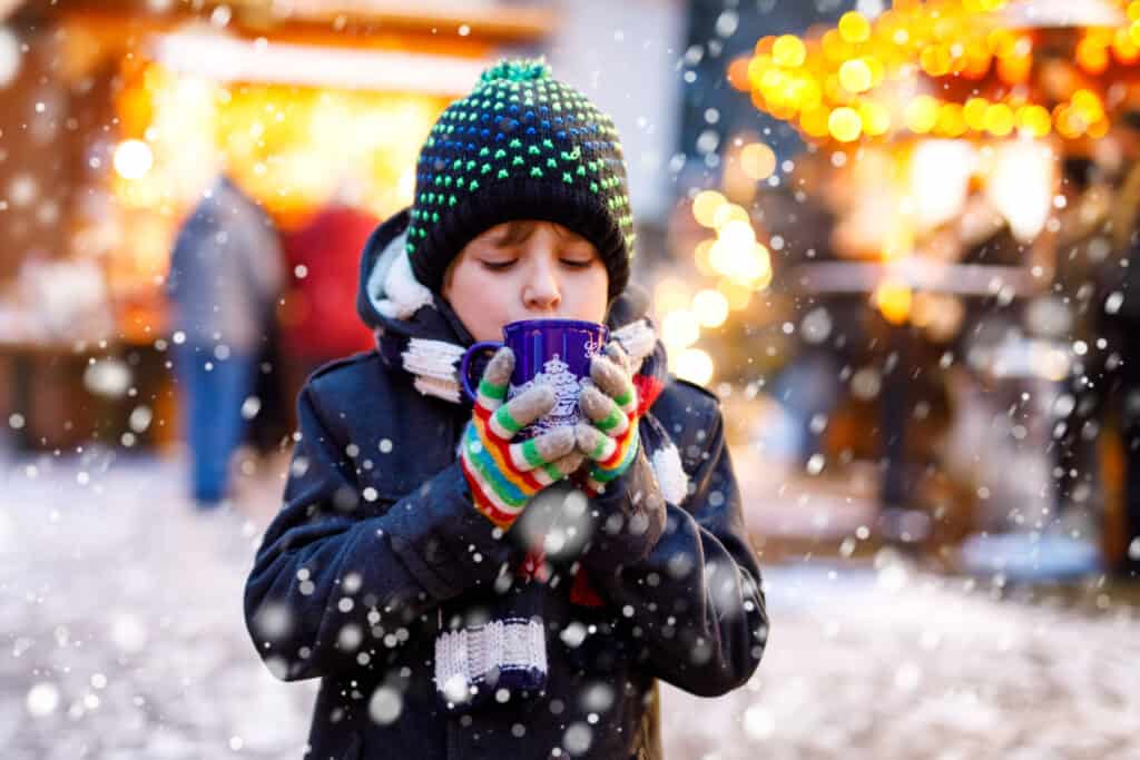 A young boy sipping from a cup at a German Christmas Market in the snow.